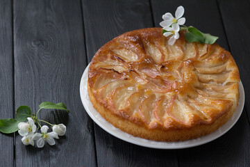 Freshly baked apple pie on a white plate with apple tree flowers on a black table. 