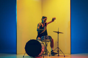 Freedom. Young musician with drums performing on yellow background in neon light. Concept of music,...