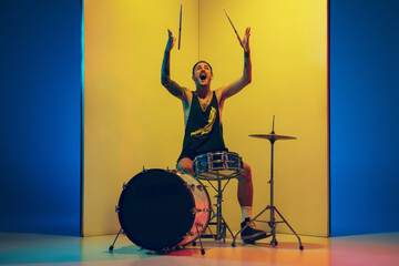 Freedom. Young musician with drums performing on yellow background in neon light. Concept of music,...