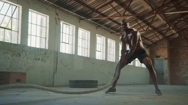 Fit man exercising with battling ropes inside old factory. Muscular man working out in cross training gym.
