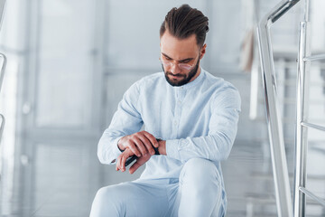 Sitting on the stairs. Young handsome man in formal clothes indoors in the office at daytime