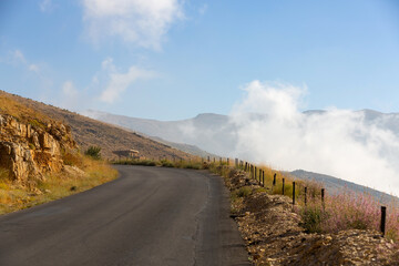 Fototapeta na wymiar Asphalt road in the mountains of Lebanon, in the Kadisha Valley. The road to the pass in the clouds. Blue sky, sunlight and white clouds