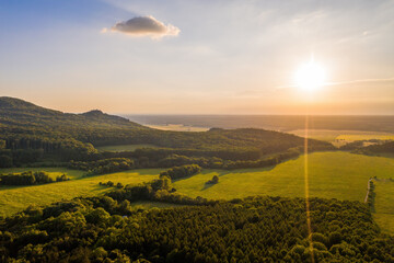 Sun shining over forested hills of Little carpathians on summer evening with a view on Zahorie area, Slovakia, Europe. Green landscape scenery from aerial perspective.