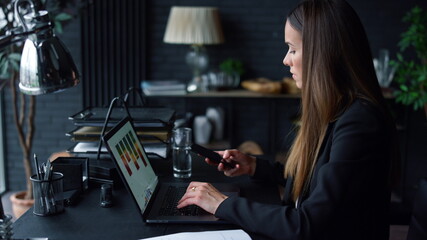 Naklejka na ściany i meble Businesswoman working on laptop at office. Employee using smartphone