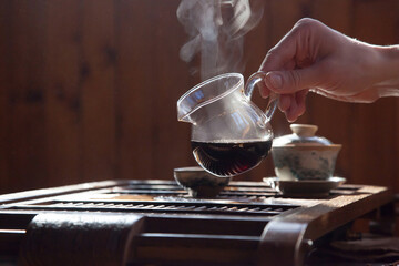 Hand pouring black chinese tea from a glass teapot with a cloud of steam