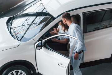 Positive young girl have a visit in autosalon and choosing car. Manager helping her