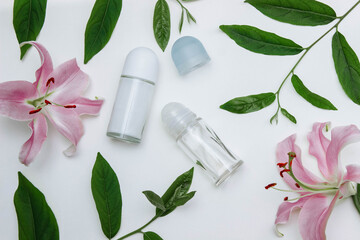 Roller deodorants in a transparent glass bottle with an open and closed lid with green leaves and pink flowers LIII on a white background top view, skin care concept, sweat protection and advertising 