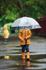 Two kids with umbrella in yellow waterproof cloaks and boots playing outdoors after the rain together © standret