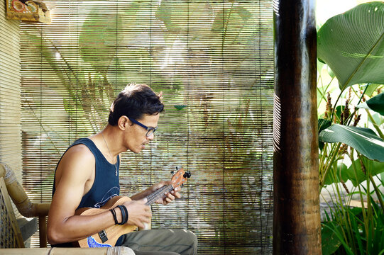 Man playing a ukulele outside a jungle bungalow