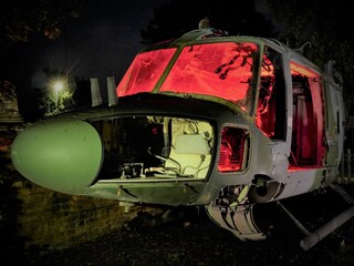 disused abandoned Helicopter grounded at night with red lighting to show nose body component parts and lit windows 