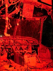 Internal cockpit of disused abandoned Helicopter grounded at night with red lighting to show controls wiring and component parts 