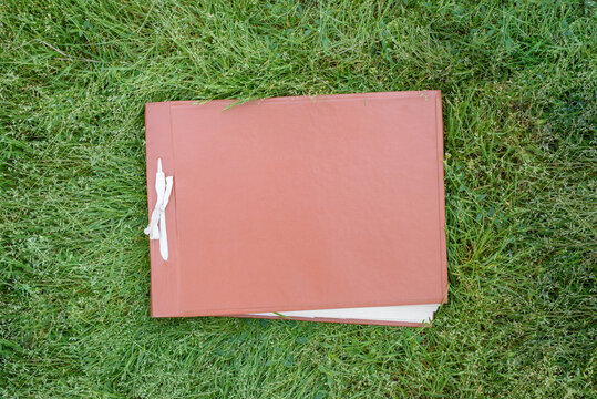 An old faded closed photo album or photo book with a red cover on the green grass on the lawn. Copy space, minimal style, the concept of storing memories.