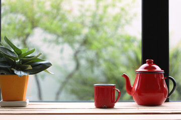 Red tea pot with red cup and plant on brown wooden table