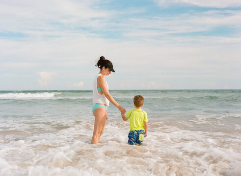 Mother leading a young boy out into an ocean