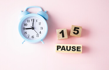Wooden blocks with the text: Pause 15 on a pink background and a blue alarm clock.