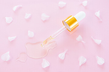 Cosmetic pipette with oil on pink background close-up. Around - flower petals. Stylish concept of organic essences, beauty and health products. Copy space, minimalism, flat lay. Modern apothecary.