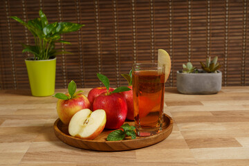 Apple juice and red apple on a wooden tray.