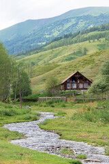 Fototapeta na wymiar A fast mountain stream and a wooden house on a background of mountains, Altai Siberia