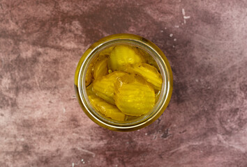 Hamburger dill pickles in a jar on a maroon table