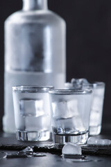 Vodka in shot glasses on black stone background, iced strong drink in misted glass
