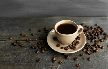 Coffee cup with roasted coffee beans on wooden table background. Mug of black coffe with scattered coffee beans on a wooden table. Fresh coffee beans.