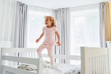 Jumping on the bed. Cute little girl in casual clothes is indoors at home at daytime