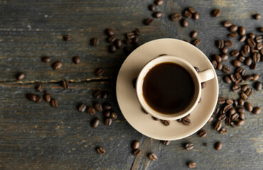 Coffee cup with roasted coffee beans on wooden table background. Mug of black coffe with scattered coffee beans on a wooden table. Fresh coffee beans.