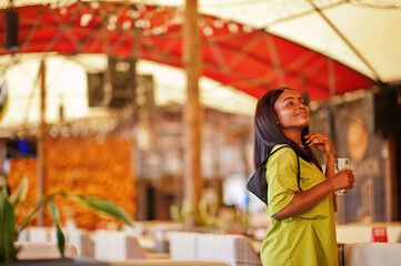 Black women wear in green summer clothes pose in tent cafe. African american girl with lemonade.