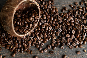 Roasted arabica coffee beans scattered on a wooden table from a coconut. Fresh coffee beans.