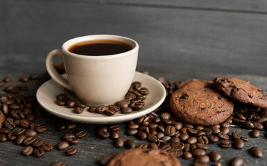 Coffee cup with cookies on wooden table background. Mug of black coffee with scattered coffee beans and cookies on a wooden table. Fresh coffee beans.