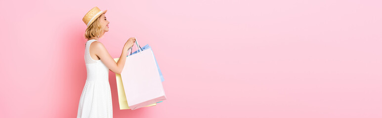 panoramic concept of young woman in white dress holding shopping bags on pink