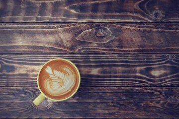 Top view, flat lay latte art coffee in a yellow cup on the old wooden table background.