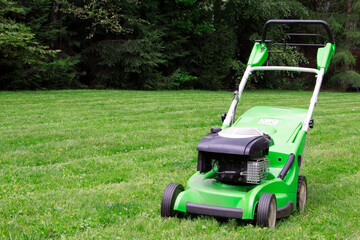 Fototapeta na wymiar A green lawnmower in the garden. A lawn mower on the green grass. Gardening