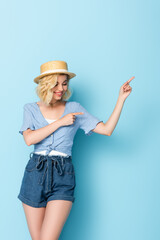 woman in straw hat pointing with fingers and looking away on blue