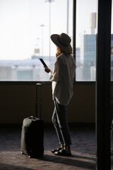 Tourist woman with hat and hand luggage waiting for the flight at the airport.