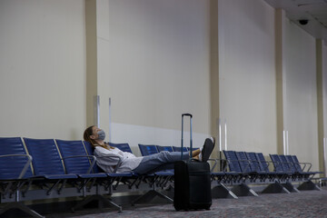 Tired tourist woman with protective medical mask waiting for the fligh at the empty airport. Traveling and safety measures during coronavirus outbreak.