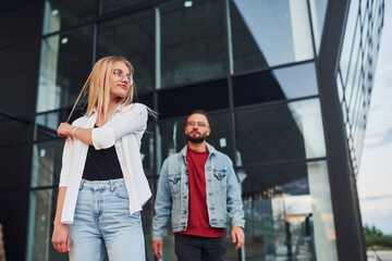Young stylish man with woman in casual clothes outdoors together near business building. Conception of friendship or relationships