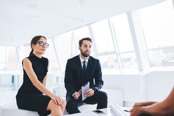 Male and female successful lawyers discussing new conditions for contract with business partners sitting in coworking space.Colleagues dressed in office outfit talking about reported financial plan