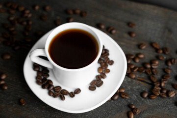 Coffee cup with roasted coffee beans on wooden table background. Mug of black coffe with scattered coffee beans on a wooden table. Fresh coffee beans.