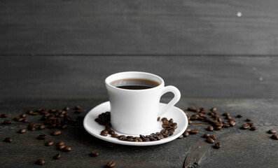 Coffee cup with roasted coffee beans on wooden table background. Mug of black coffe with scattered coffee beans on a wooden table. Fresh coffee beans.