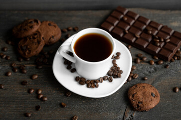 Coffee cup with cookies and chocolate on wooden table background. Mug of black coffee with chocolate cookies. Fresh coffee beans.