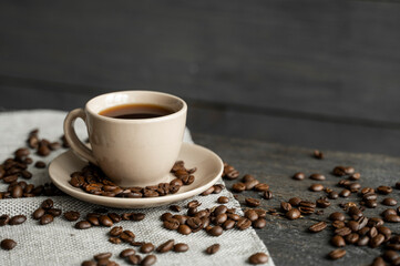 Coffee cup with roasted coffee beans on wooden table background. Mug of black coffe with scattered...