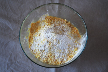transparent glass round bowl with corn and rice flour on a beige tablecloth top view.  Ingredients before baking gluten-free at home
