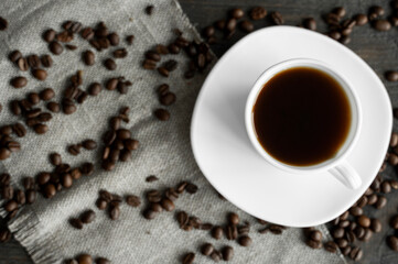 Coffee cup with roasted coffee beans on wooden table background. Mug of black coffe with scattered coffee beans on a wooden table. Fresh coffee beans.