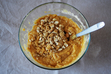 cashews, banana, coconut oil and egg while stirring with a metal spoon in a glass bowl on the table in the kitchen.  making banana cake gluten-free and lactose-free