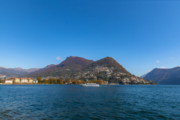 Stunning  panorama view of Lugano Lake, cityscape of Lugano, mountain Monte Bre and Swiss Alps on a sunny autumn day with blue sky cloud, cruise ship in foreground, Canton of Ticino, Switzerland