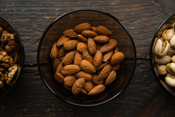 Almond, pistachio and walnut in a small plates which standing on a black table. Nuts is a healthy vegetarian protein and nutritious food.