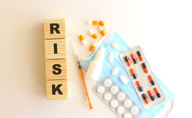 The words RISK is made of wooden cubes on a white background with medical drugs and medical mask. Medical concept.