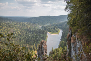 High single rock in the form of a column, next to other rocks on the background of the river and forest