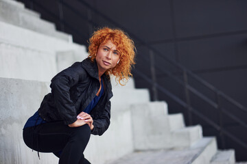 Young european redhead woman in sportive clothes doing exercises on stairs outdoors